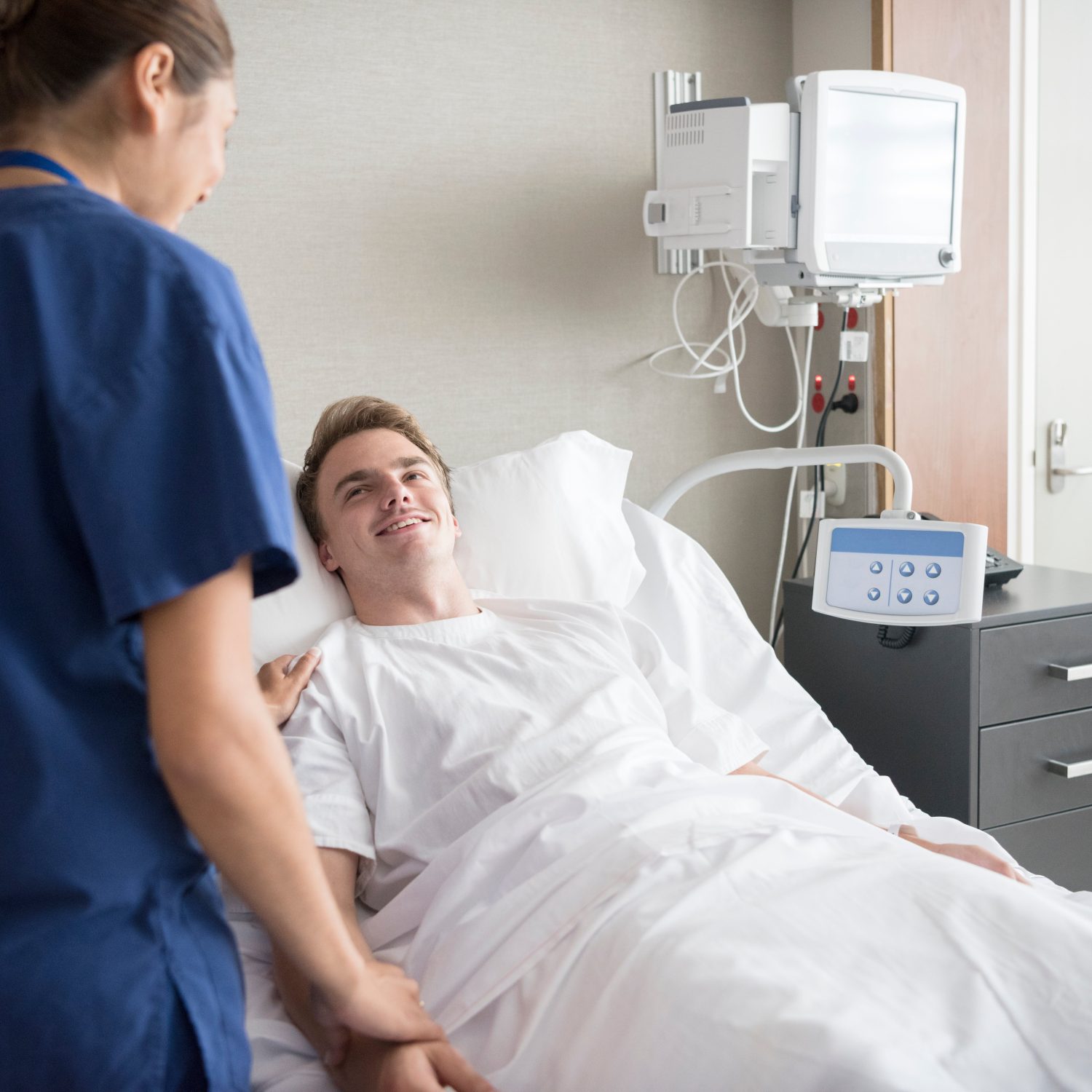 Medical staff in hospital caring for young man in bed. Man smiling in hospital bed, nurse with hand on his shoulder.